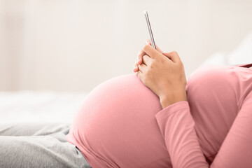 Unrecognizable pregnant woman using smartphone in bedroom, side view, free space