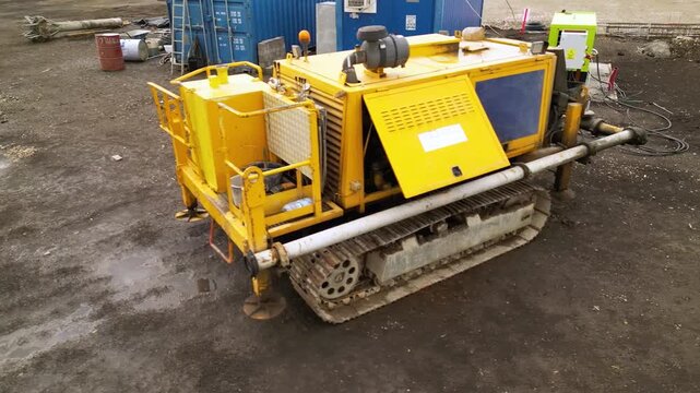 Aerial view of a compact tracked industrial machine operating beside a portable power unit and temporary site cabin, showing heavy-duty equipment used for construction, drilling or ground engineering 