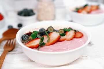 Presented by fruits putting yogurt toppings with strawberry, berry, oats, raisins and chia seed decorated by peppermint in white blow. Pink background. Set of healthy dairy product choice. Pecuniary.