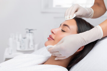 Hands of skillful beautician cleaning and touching female face with cotton pads or sponges. Woman...