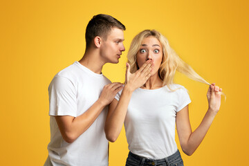 Unbelievable. Guy whispering secret or gossip to surprised girl, yellow background with copy space