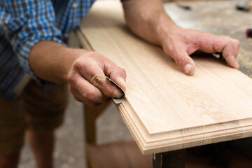 The carpenter grinds the edge of the oak board with sandpaper