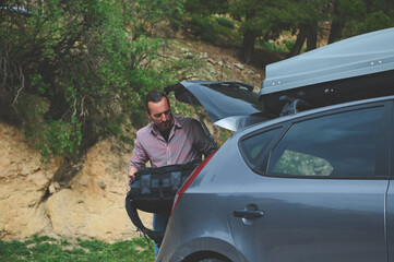 Man unloading car trunk during outdoor adventure trip in nature