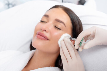 Closeup of young European woman receiving hyaluronic acid injection in cheekbones at beauty salon, enjoying beauty procedures