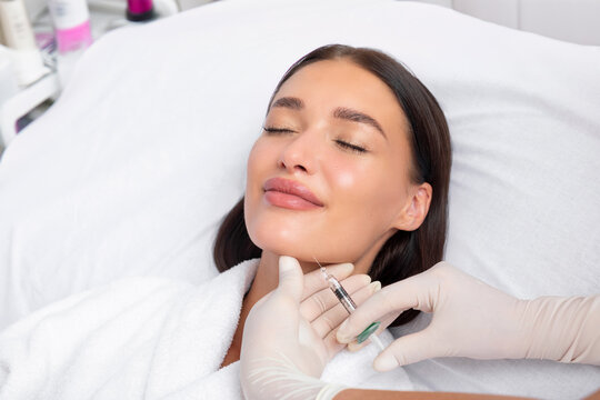 Cosmetologist making lipolytic injections to burn fat on the chin, cheeks and neck of woman in beauty salon. Cosmetology concept