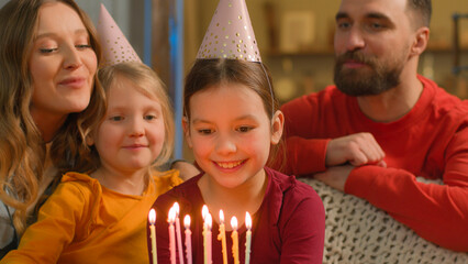 Caucasian family sing happy birthday little girl child daughter blow cake candles wish celebration...