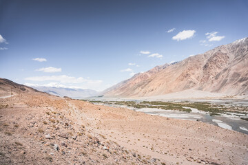 Pyanj River flows in Wakhan Valley among rocky high mountains against snow-capped peaks and glaciers in Tajikistan's Tien Shan mountains, landscape for background