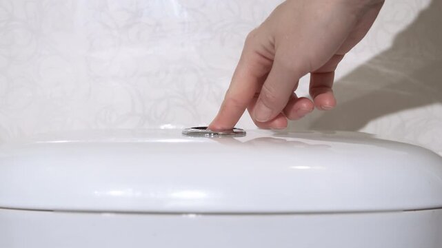 Female pressing the flush button. A view of woman hand pressing the flush button on toilet in the clean bath.