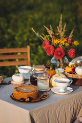 Tea setting with handmade pie. Beautiful view of garden wooden furniture with basket, soft blanket and burning candles. Outdoors fall family party, cozy autumn interior. Pumpkins, red dahlia