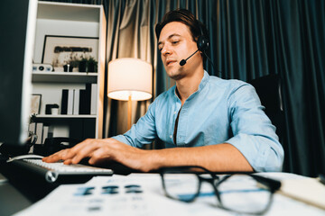 Call center consulting with customers on headphones on monitor in business paragraph with typing on pc with dynamic data marketing analysis planning at modern home office at night time. Pecuniary.