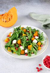 Pumpkin salad with arugula, feta cheese, pomegranate seeds on gray background. Top view. Thanksgiving Dishes. 