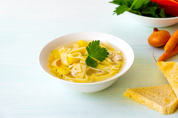 Chicken soup with noodles and vegetables in white bowl