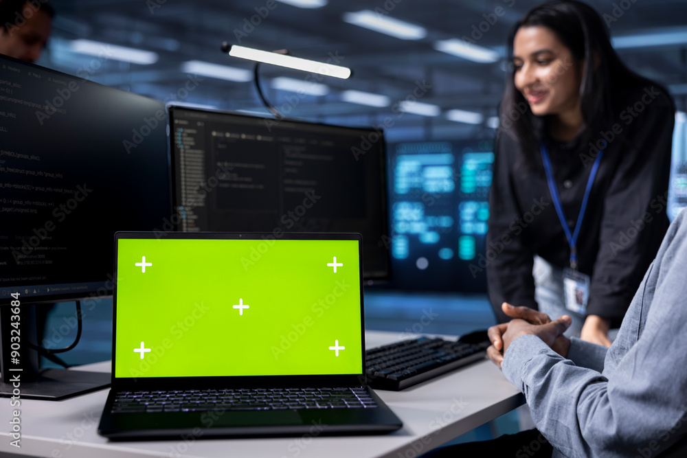 Poster focus on green screen notebook used by engineers in blurry background to oversee servers used for ma