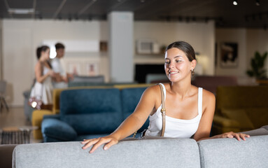 Young woman chooses comfortable sofa in department of furniture store