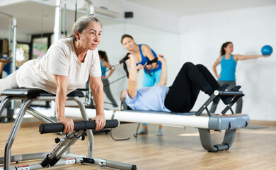 Old woman training on Pilates Wanda chair machine during her health exercise in rehabilitation studio