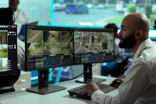 Middle eastern employee monitoring traffic surveillance footage on displays, using radar and CCTV system in observation room. Expert handling license plate recognition on security cameras.