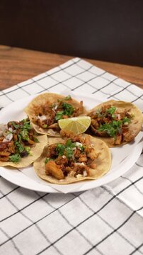 Vertical food video, four tacos al pastor served on a white plastic plate