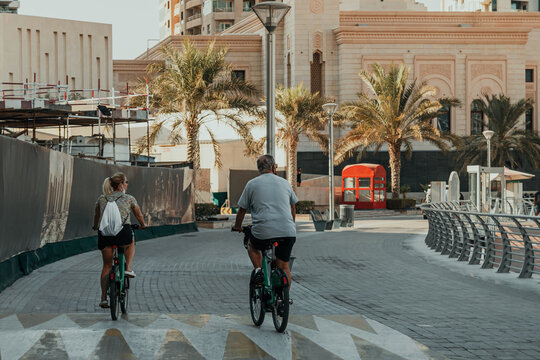 Morning waterfront promenade with palm trees and cyclists on modern marina walkway