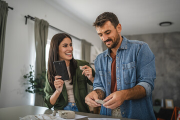 Couple learn from mobile phone how to make a clay figurine, pottery