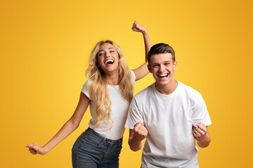 We did it. Euphoric young students celebrating successful passing exams, yellow studio background...