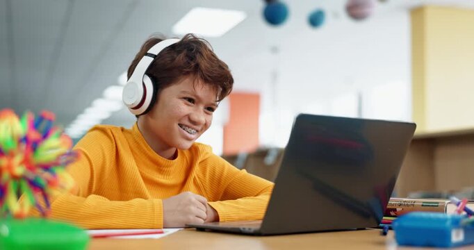 Laughing, school and boy on laptop for online class, remote education or elearning with funny joke. Library, smile or happy male child student listening in headphones on virtual teaching platform