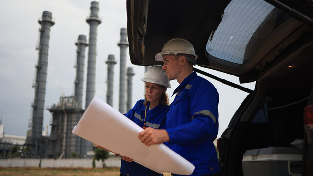 Engineer couple male  and female working with blueprint and discussion at the trunk of the car in power plant industrial  - Powered by Adobe