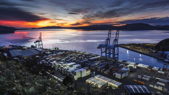 A time-lapse of Port Chalmers in Dunedin as the sun sets with a dramatic sky. Vehicles whiz around loading and stacking shipping containers