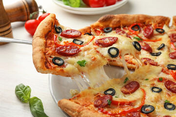 Taking piece of tasty pizza with smoked sausages, olives, pepper and parsley at light wooden table, closeup