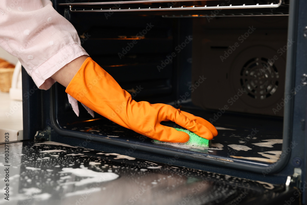 Poster Woman cleaning oven with sponge, closeup view