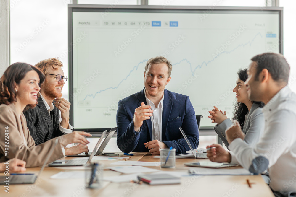 Poster A group of business professionals are gathered around a conference table in a modern office. The group is engaged in a conversation and appears to be working together on a project
