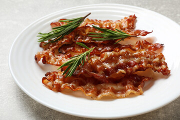 Slices of tasty fried bacon and rosemary on light grey table, closeup