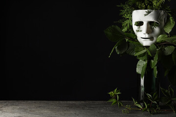Theatrical performance. Plastic mask and floral decor on table against black background, space for...