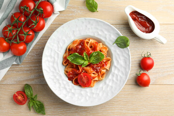 Delicious pasta with sauce, tomato and basil on wooden table, flat lay