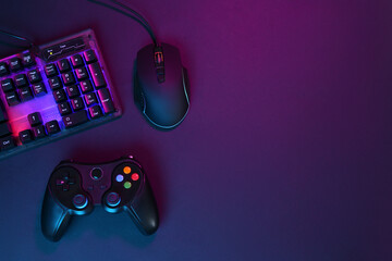 Computer mouse, RGB keyboard and game controller in neon lights on dark background, flat lay. Space...
