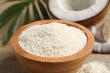 Fresh coconut flour in bowl, nut and palm leaf on white wooden table, closeup