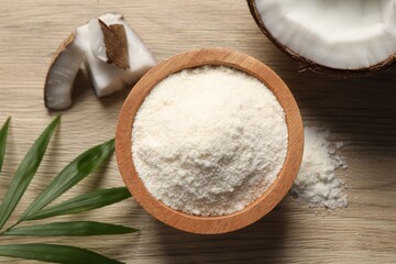 Fresh coconut flour in bowl, nut and palm leaf on wooden table, flat lay