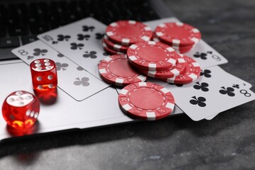 Poker chips, laptop, playing cards and dices on grey table, closeup. Online game