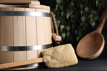 Sauna equipment. Wooden bucket, ladle and loofah on black table