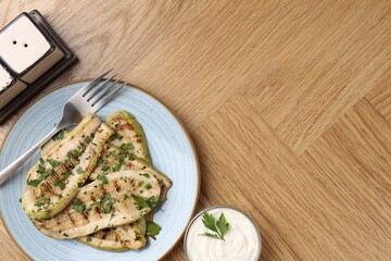 Tasty grilled courgette slices served on wooden table, flat lay. Space for text