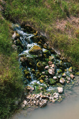 Stream in the forest in the daylights. Natural background of small waterfalls on the rocks surrounded by moss