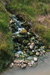 Stream in the forest in the daylights. Natural background of small waterfalls on the rocks surrounded by moss