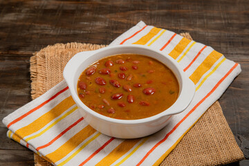 traditional colombian beans soup on white bowl over striped kitchen towel and yute