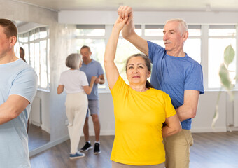 Happy smiling elderly woman enjoying impassioned merengue with male partner in latin dance class. Social dancing concept..