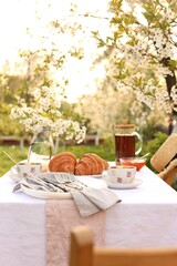 Stylish table setting with tea and croissants in spring garden