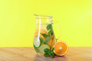 Fototapeta premium Freshly made lemonade with mint in jug on wooden table against yellow background