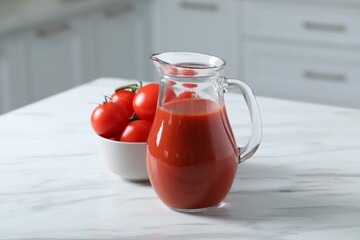 Tasty tomato juice in jug and vegetables on white marble table