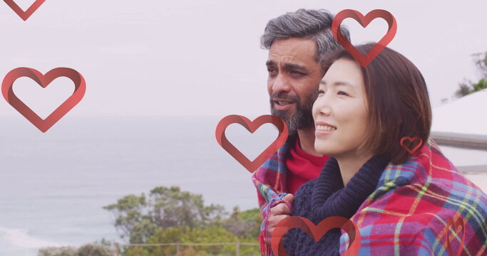 Image of hearts over diverse couple embracing on balcony - Powered by Adobe