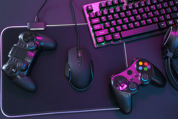 Computer mouse, RGB keyboard and game controllers in neon lights on dark background, top view © New Africa