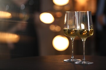 Tasty wine in glasses on black table against blurred lights, space for text