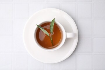 Aromatic herbal tea with sage in cup on white tiled table, top view